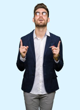 Güneş gözlüğü ve moda ceket giyen genç yakışıklı zarif adam hayret ve yukarıya bakıp parmakları ile işaret şaşırttı ve silah kaldırdı.