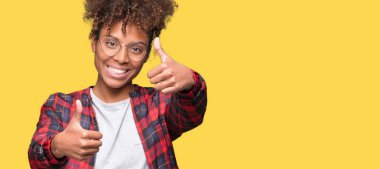 Güzel genç Afro-Amerikan kadın gözlük izole arka plan onaylama üzerinde el ile pozitif jest yapıyor gülümseyen ve başarı için mutlu başparmak. Kamera, kazanan jest arıyorsunuz.