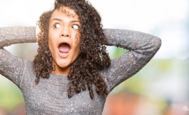 Gri kazak deli giyen ve baş, korkuyor ve açık ağzı ile şok sürpriz elleriyle korkuttu kıvırcık saçlı genç güzel kadın