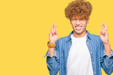 Umut ve gözleri kapalı geçiş parmaklarıyla gülümseyen denim ceket giyen afro saçlı Genç yakışıklı adam. Şans ve batıl kavramı.