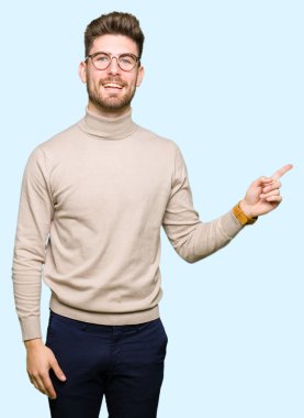 Kameraya bakarak yan el ve parmak ile işaret yüzünde, kocaman bir gülümseme ile gözlük takan genç yakışıklı iş adamı.