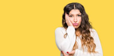 Beyaz kazak düşünme seyir giyen genç güzel kadın yorgun ve sıkılmış çapraz silah depresyon sorunları ile.