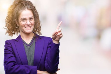 Yüzünde kocaman bir gülümseme ile izole arka plan üzerinde okul üniforması ve gözlük giyen genç esmer öğrenci kız kameraya bakarak yan el ve parmak ile işaret.