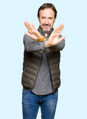 Orta yaş yakışıklı adam giyen kış yelek ret ifade geçiş silah ve avuç içi eksi işareti, kızgın surat yapıyor