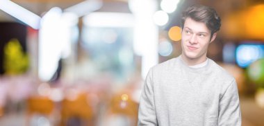 Genç yakışıklı sportif adam kazak giyiyor görünümlü yan ve dik dik bakma uzağa düşünce gülümseyen izole arka plan üzerinde.