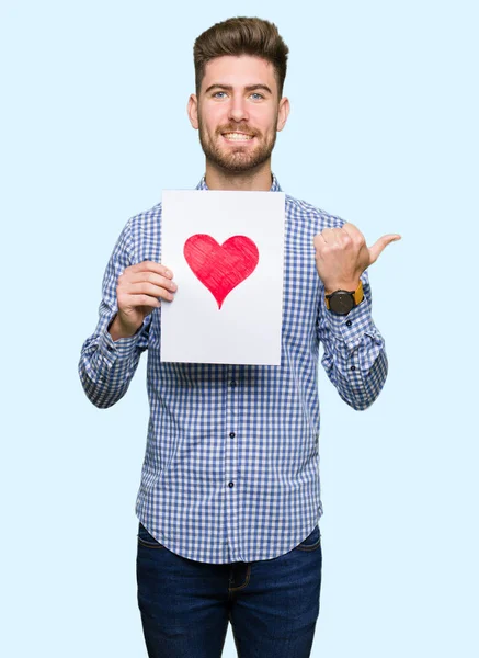 Jovem Homem Bonito Segurando Papel Com Coração Vermelho Apontando Mostrando — Fotografia de Stock