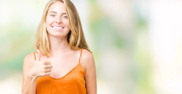美丽的年轻女子穿着橙色衬衫在孤立的背景做快乐的大拇指与手的手势 查看显示成功的相机的审批表情 — 图库照片
