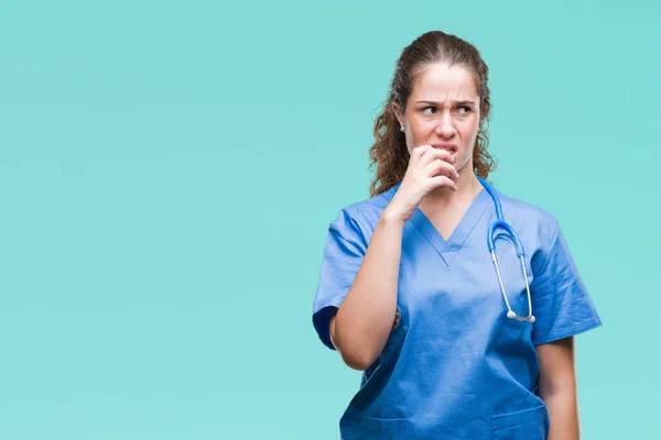 年轻的黑发医生女孩穿着护士或外科医生制服在孤立的背景看起来紧张和紧张的手在嘴咬指甲 焦虑问题 — 图库照片