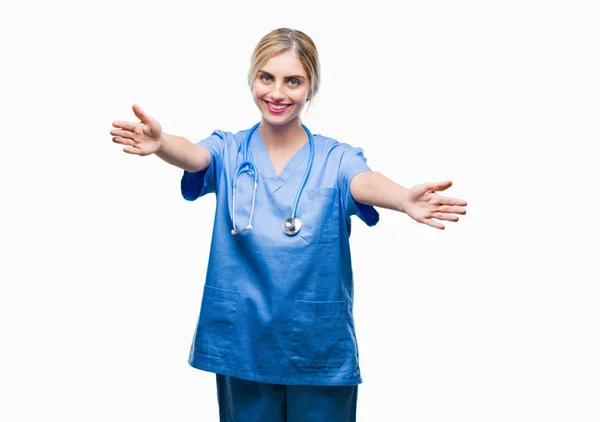若い美しい金髪の医者の外科医看護師女性抱擁の両手を広げて笑みを浮かべてカメラを見て孤立の背景の上 晴れやかな表情の受け入れ幸せ — ストック写真