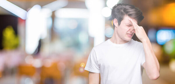 Young handsome man wearing casual white t-shirt over isolated background smelling something stinky and disgusting, intolerable smell, holding breath with fingers on nose. Bad smells concept.