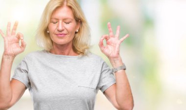 Orta yaş sarışın kadın izole arka plan üzerinde dinlenmek ve gülümseyen gözlerle parmak ile meditasyon jest yapıyor kapalı. Yoga kavramı.
