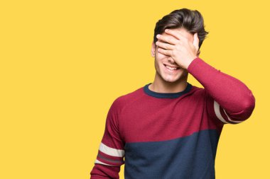 Yakışıklı genç gülümseyen ve gözler için sürpriz kapsayan yüz el ile gülüyor izole arka plan üzerinde. Kör kavramı.