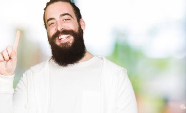 Uzun saç ve sakal sportif kazak gösterme ve kendinden emin ve mutlu gülümseyen bir parmak ile işaret eden oktan yukarı giyen genç adamla.