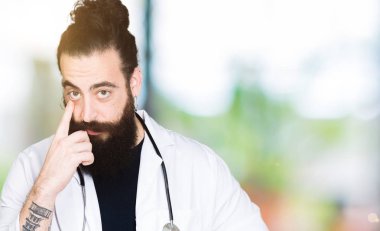 Doktor stetoskop tıbbi ceket giyen uzun saçlı göz izlerken seni jest için şüpheli ifade işaret