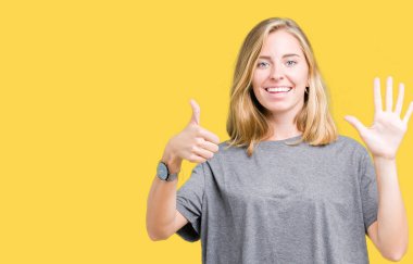 Gösterilen ve parmakları ile işaret izole arka plan üzerinde büyük boy rahat t-shirt giyen güzel genç kadın kendinden emin ve mutlu gülümseyerek süre 6 numara.