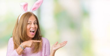 Paskalya tavşan kulakları hayrete ve el ile sunulması ve parmak ile işaret ederken kameraya gülümseyen izole arka plan üzerinde giyen orta yaş esmer kadın.