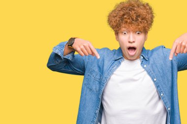 Afro saçlı kot giyen genç yakışıklı adam aşağı reklam, sürpriz yüz ve açık ağız gösterilen parmakları ile işaret ceket