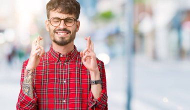 Umut ve gözleri kapalı geçiş parmaklarıyla gülümseyen izole arka plan üzerinde gözlük takan yakışıklı delikanlı. Şans ve batıl kavramı.