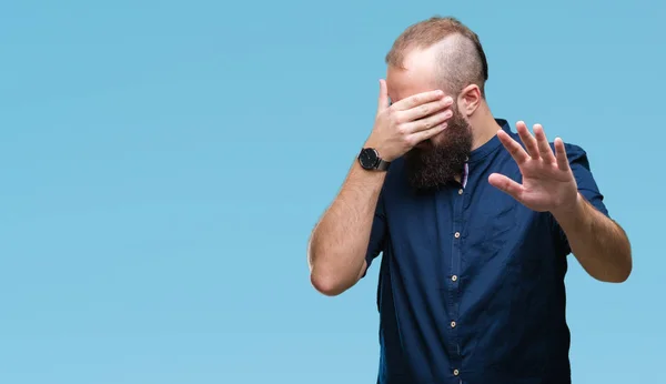 Young caucasian hipster man over isolated background covering eyes with hands and doing stop gesture with sad and fear expression. Embarrassed and negative concept.
