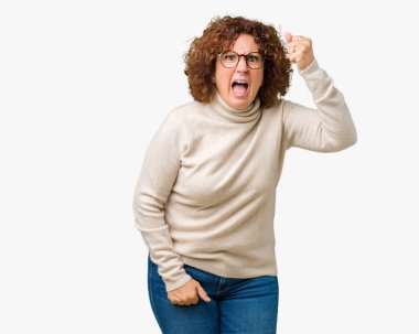 Boğazlı kazak ve gözlük kızgın ve kızgın izole arka plan üzerinde giyen güzel orta ager üst düzey kadın hayal kırıklığı ve öfke ile bağırarak süre öfkeli yumruk yükselterek. Öfke ve agresif kavramı.