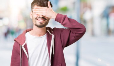 Yakışıklı genç gülümseyen ve gözler için sürpriz kapsayan yüz el ile gülüyor izole arka plan üzerinde. Kör kavramı.