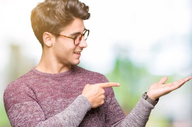 Hayret ve el ile sunulması ve parmak ile işaret ederken kameraya gülümseyen izole arka plan üzerinde gözlük takan genç yakışıklı adam.