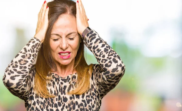Beautiful middle age woman wearing leopard animal print dress suffering from headache desperate and stressed because pain and migraine. Hands on head.