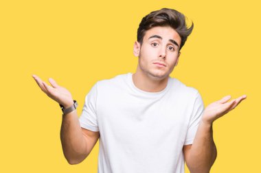 Üzerinde beyaz t-shirt giyen genç yakışıklı adam arka plan clueless ve şaşkın bir ifadeyle kollar ve eller kaldırdı izole. Şüphe kavramı.