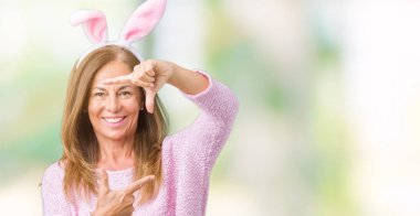 Paskalya tavşan kulakları elle yapma çerçeve ve parmakları ile mutlu yüz gülümseyen izole arka plan üzerinde giyen orta yaş esmer kadın. Yaratıcılık ve Fotoğrafçılık kavramı.