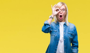 Sürpriz yüz, parmaklarının arasından seyir göz gözlük ok jest yapıyor izole arka plan üzerinde giyen genç güzel sarışın kadın şok. İmansız ifade.