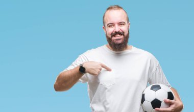 Sürpriz yüz işaret parmağı kendini izole arka plan üzerinde futbol futbol topu tutan genç beyaz hipster adam