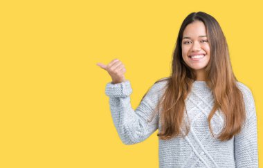 Seyir ve başparmak yanında yukarıyı mutlu yüz ile gülümseyen izole arka plan üzerinde kazak giyen genç güzel esmer kadın.