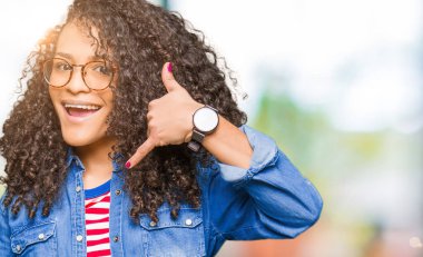 Kıvırcık saçlı gözlüklü yapıyor gülümseyen genç güzel kadın telefon hareketi ile el ve parmak telefonda konuşuyor gibi. Kavramları iletişim.