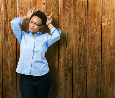 Neşeli gülümseyen genç güzel Afro-Amerikan iş kadını komik ve çılgın baş parmaklar ile kulakları, tavşan poz izole arka plan üzerinde