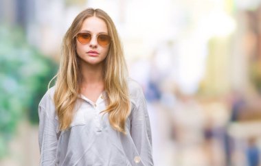 Genç güzel sarışın kadın yüzünde ciddi bir ifade ile izole arka plan üzerinde güneş gözlüğü takıyor. Basit ve doğal kameraya bakıyor.