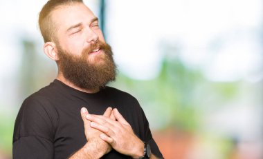 Göğüs kapalı gözler ve yüzünde minnettar jest ile gülümseyen rahat t-shirt giyen genç sarışın adam ellerini. Sağlık kavramı.