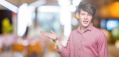 Genç yakışıklı iş adamı neşeli sunulması ve kameraya bakarak avucunun ile işaret gülümseyen izole arka plan üzerinde.