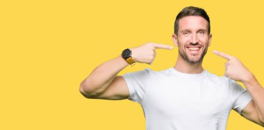 Yakışıklı adam kendinden emin gösterilen ve işaret parmakları diş ve ağız ile gülümseyen casual beyaz t-shirt giyiyor. Sağlık kavramı.