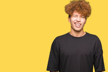 Afro saçlı siyah t-shirt göz kırpıyor seksi bir ifadeyle, neşeli ve mutlu yüzünü kameraya bakarak giyen genç yakışıklı adam.