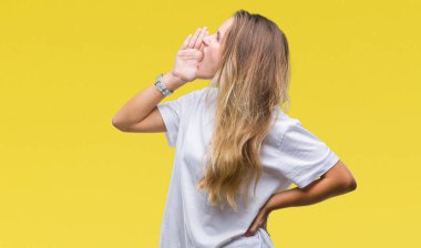 Bağırarak ve ağzı üzerinde el ile yan için çığlık izole arka plan üzerinde rahat beyaz t-shirt giyen genç güzel sarışın bir kadın. İletişim kavramı.