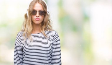 Yüzünde ciddi bir ifade ile izole arka plan üzerinde kulaklık ve güneş gözlüğü giyen güzel genç sarışın kadın. Basit ve doğal kameraya bakıyor.