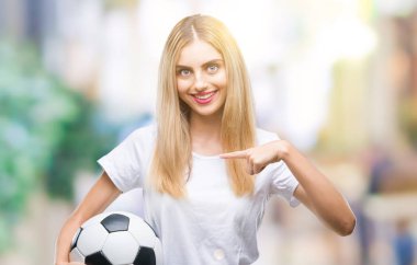 Sürpriz yüz işaret parmağı kendini izole arka plan üzerinde futbol topu tutan genç güzel sarışın kadın