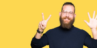 Gözlük ve gösterilen ve parmakları ile işaret boğazlı kazak giyen genç sarışın adam kendinden emin ve mutlu gülümseyerek süre yedi numara.