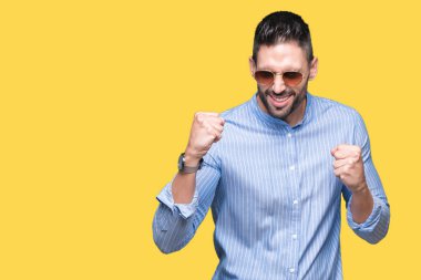 Yakışıklı delikanlı üzerinde güneş gözlüğü takıyor arka plan çok mutlu ve heyecanlı kaldırdı, silah ile kazanan jest yapıyor gülümseyen ve başarı için çığlık izole. Kutlama kavramı.