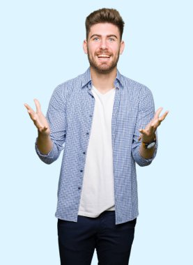 Genç yakışıklı sarışın adam giyiyor rahat gömlek kutluyor deli ve çığlık kaldırdı ve açık gözleri hayret silah ile başarı için heyecanlı. Kazanan kavramı