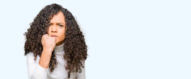 Genç güzel kadın kıvırcık saçlı öfkeli ve sinirli sinirli ve öfke ile bağırarak süre öfkeli yumruk yükselterek boğazlı kazak giyiyor. Öfke ve agresif kavramı.