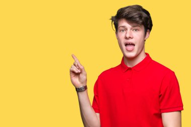 Kameraya bakarak yan el ve parmak ile işaret yüzünde kocaman bir gülümseme ile izole arka plan üzerinde kırmızı t-shirt giyen genç yakışıklı adam.