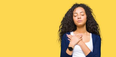 Kıvırcık saçları ile gülümseyen genç güzel kız göğüs kapalı gözler ve yüzünde minnettar jest ile eller. Sağlık kavramı.