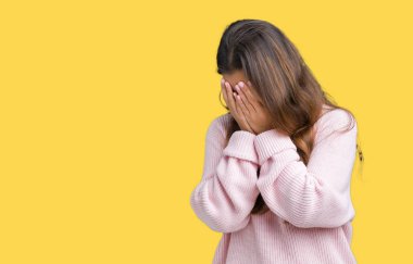 Yüzünü elleriyle ağlayarak süre kapsayan üzgün ifade ile izole arka plan üzerinde pembe kış kazak giyen genç güzel esmer kadın. Depresyon kavramı.