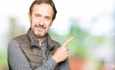 Orta yaş yakışıklı adam giyen kış reklam, ciddi ve sakin yüz gösterilen yan el parmak ile işaret yelek